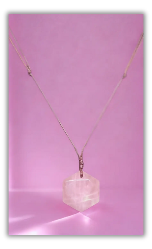 A delicate rose gold chain necklace featuring a faceted, polished pale pink gemstone pendant, displayed against a solid pink background.